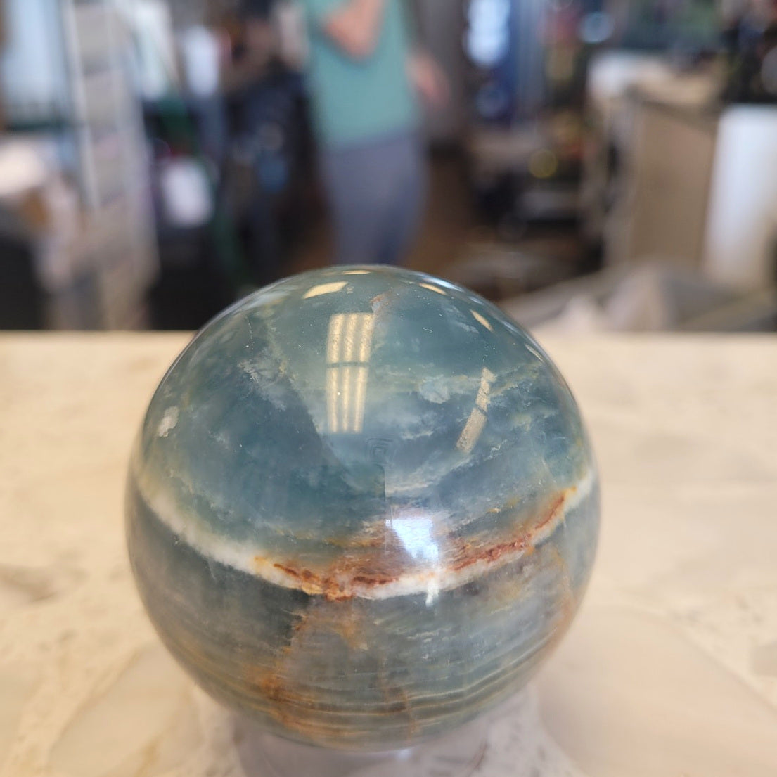 56.7mm Blue Onyx sphere in ambient indoor light showing natural blue and cream coloring