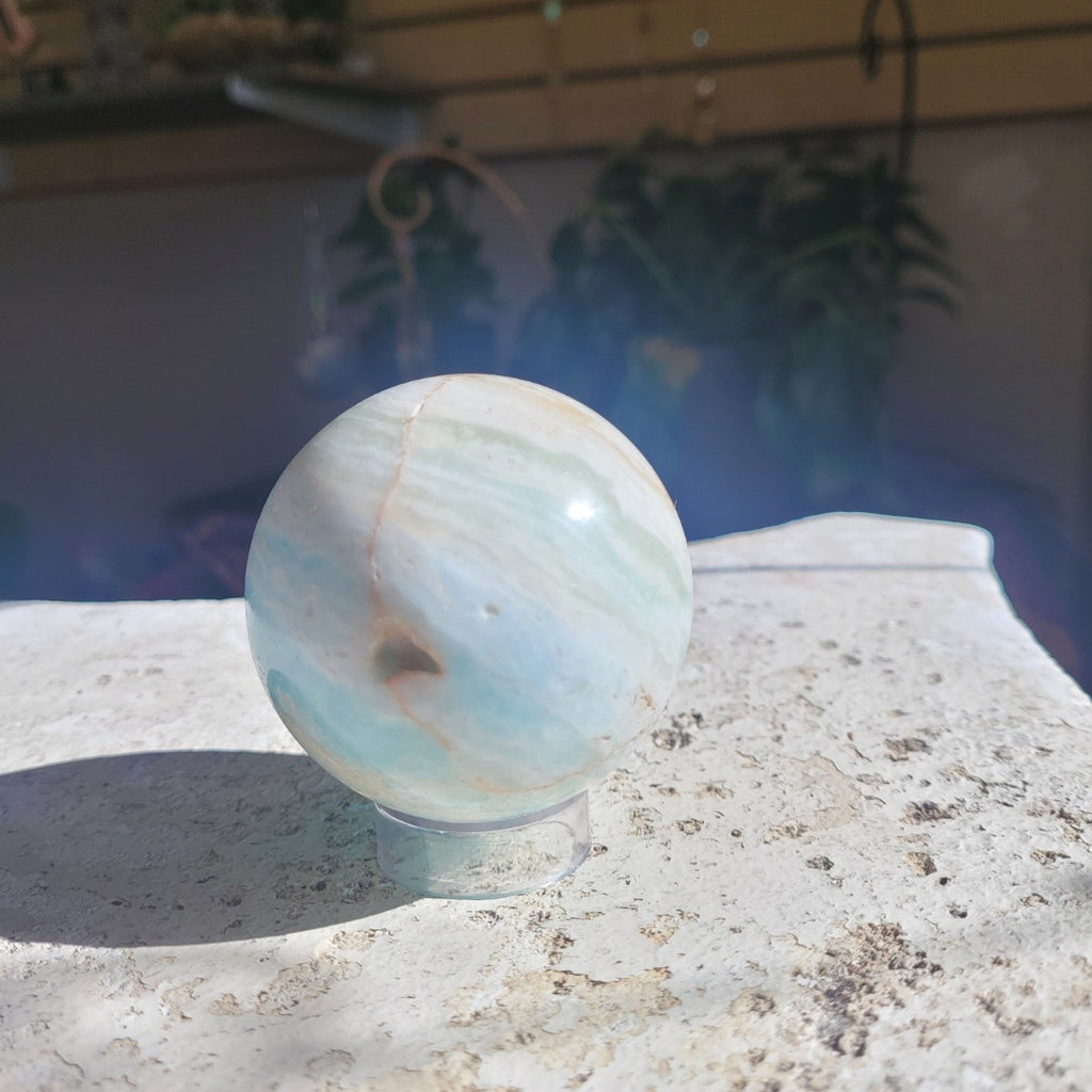 Natural Caribbean Calcite sphere showing seafoam banding and a small mineral cavity