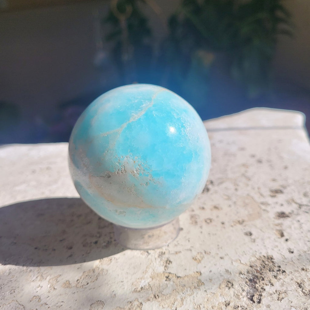 62mm Caribbean Calcite sphere in sunlight showing bright aqua blue and natural cream banding