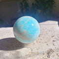 62mm Caribbean Calcite sphere in sunlight showing bright aqua blue and natural cream banding
