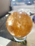 69.3mm Golden Healer Quartz sphere in natural sunlight showing honey-gold color and internal crystalline planes